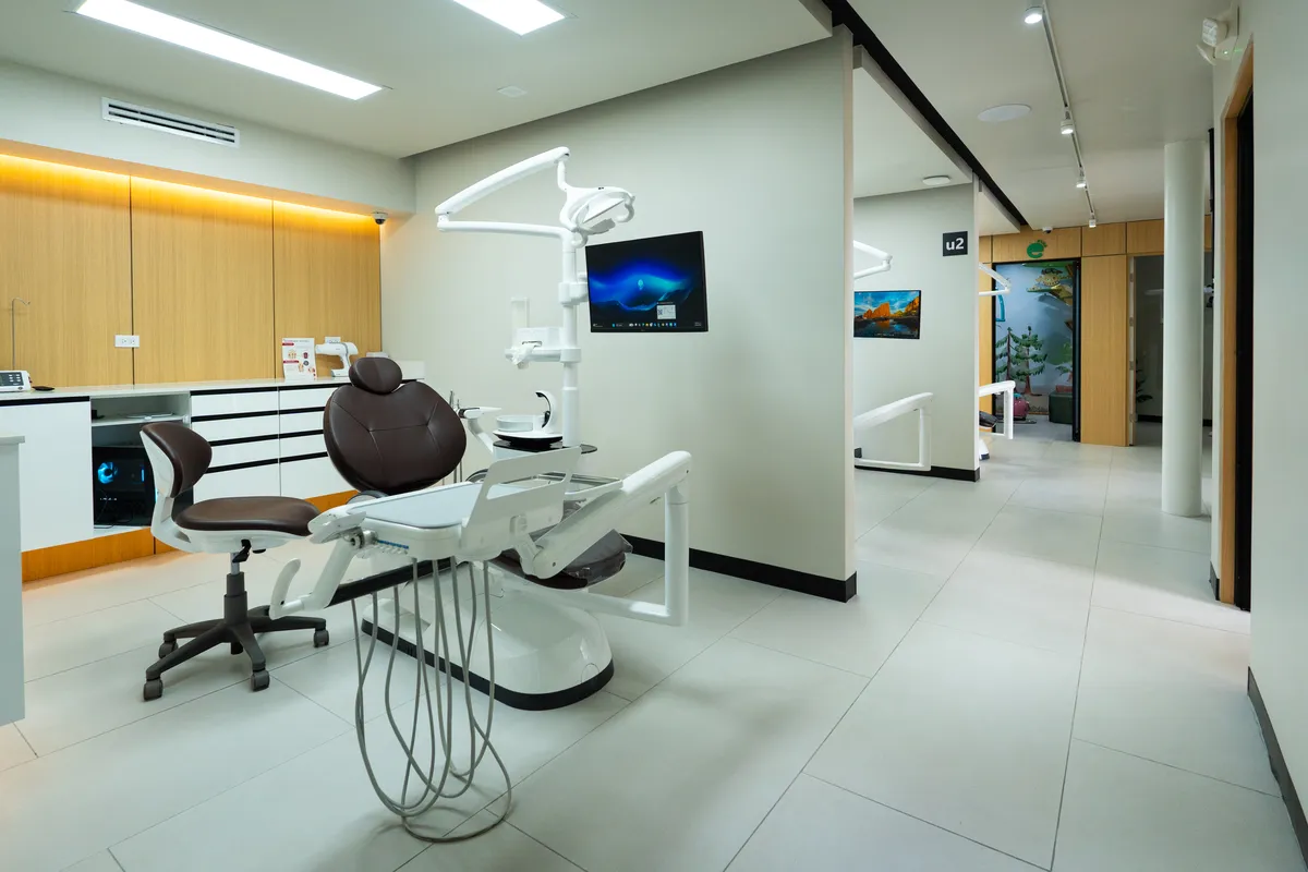 A modern and clean dental operatory room at Let's Smile Dentistry in Mexicali. The clinic features an advanced white and brown dental chair, digital monitors, custom wooden cabinetry, and a bright, minimalist hallway leading to private treatment cubicles.